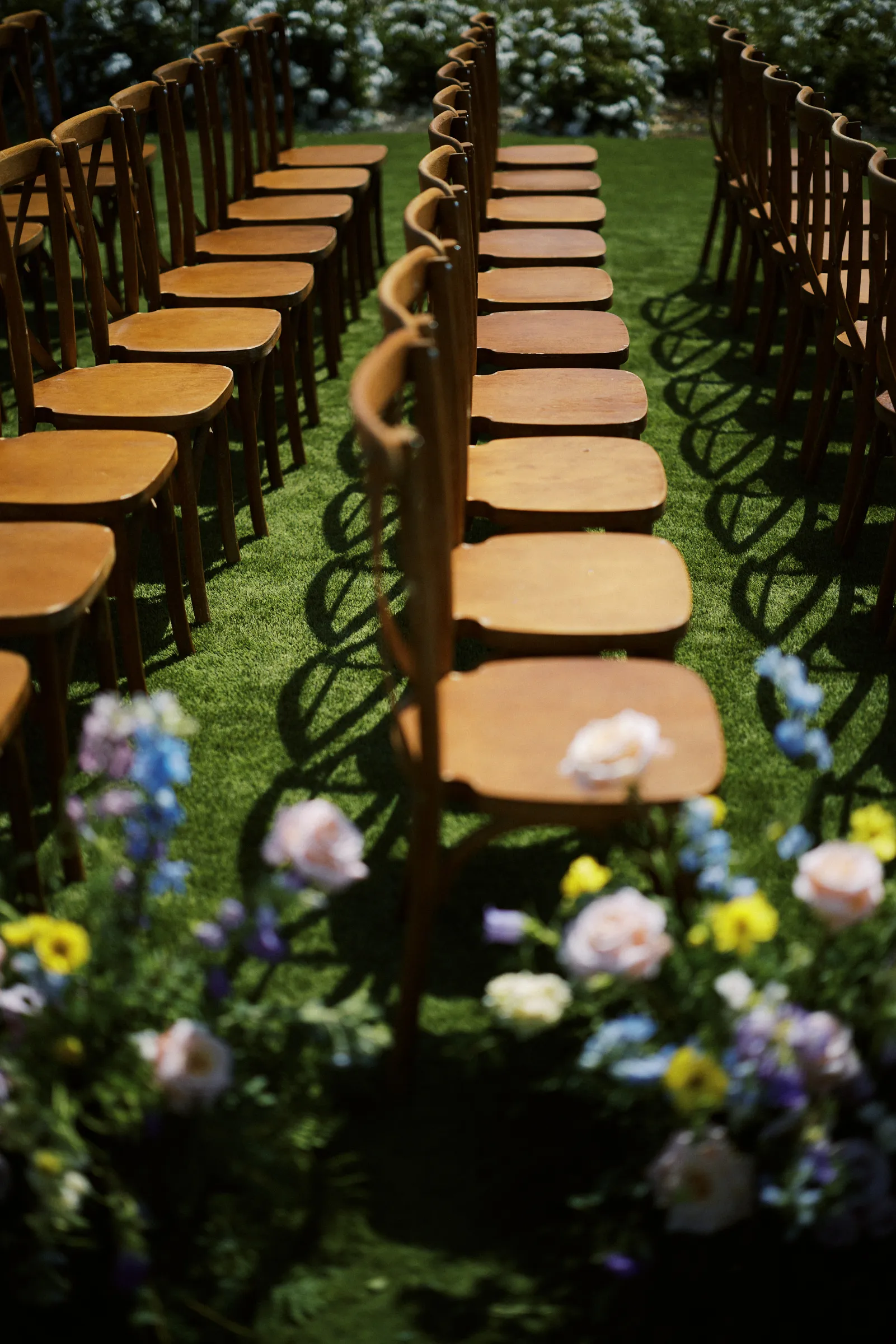 Rows of wooden ceremony chairs lined with wildflowers