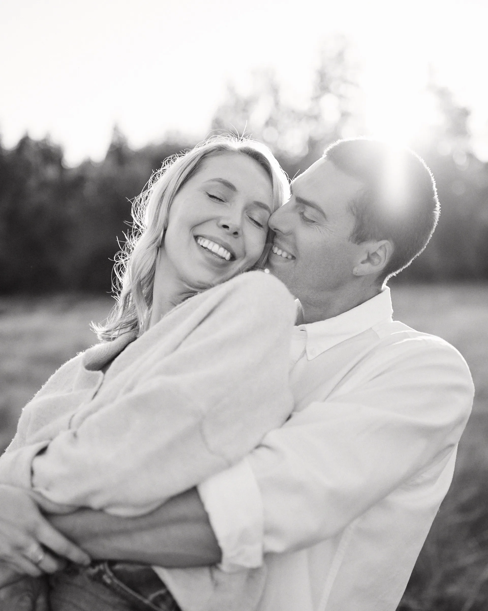 A couple laughing in an embrace, backlit by the low sun, in black and white