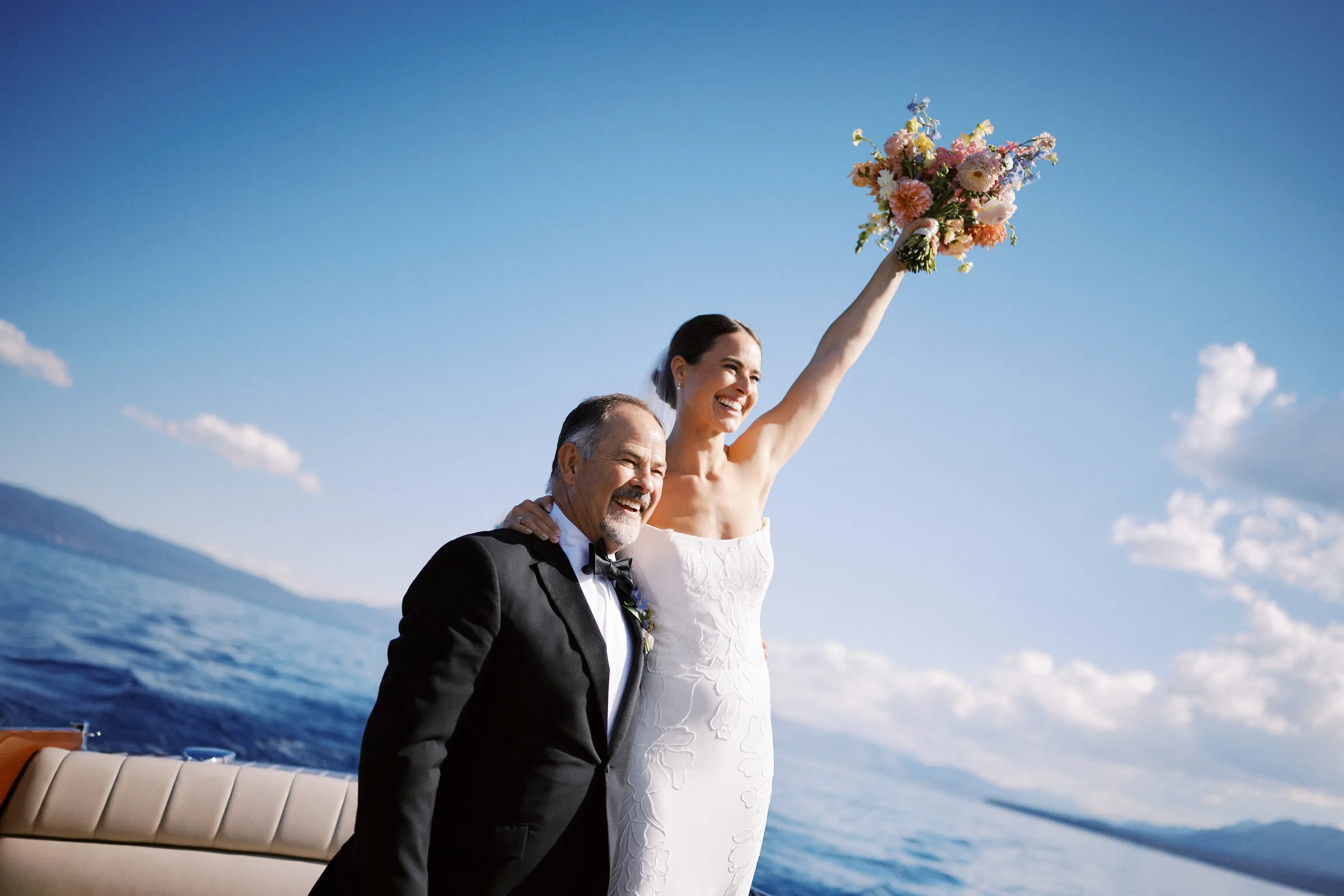 The bride raising her bouquet from a wooden boat on the lake
